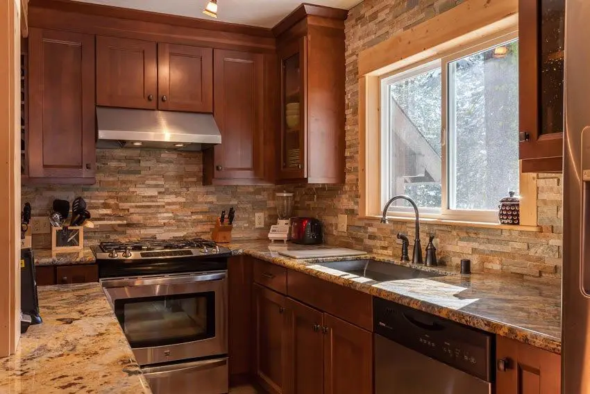 Small craftsman galley kitchen with stacked stone backsplash, brown cabinets and beige granite countertops