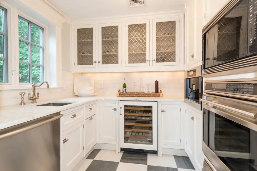 Small galley kitchen with white cabinets with glass pane doors, carrara marble counter and black and white checkered floors