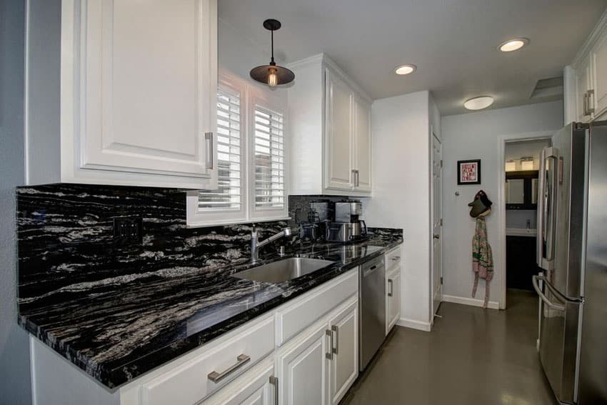 Small traditional galley kitchen with white raised panel cabinets and black space granite counter