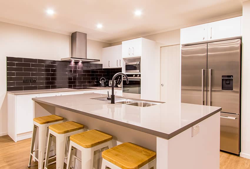 Kitchen with black backsplash tiles, recessed lighting and chairs with wood seats