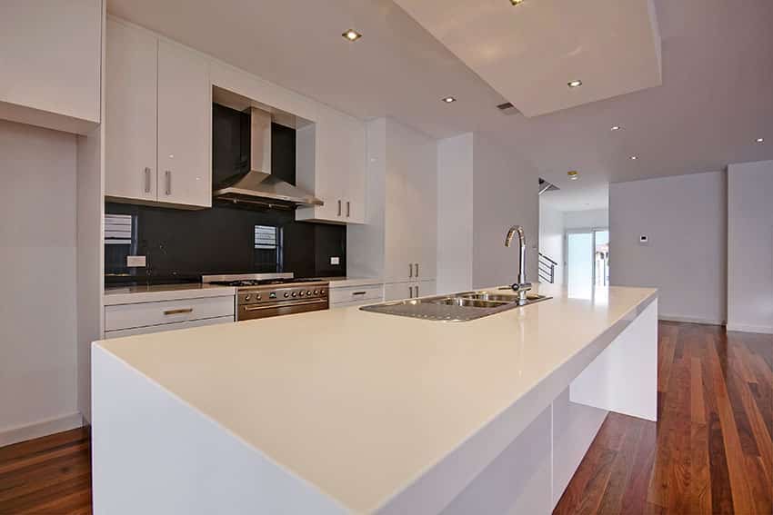 White modern kitchen with black glass backsplash and white island with sink