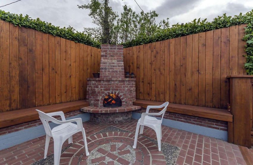 Wood fence surrounding backyard brick patio with fireplace