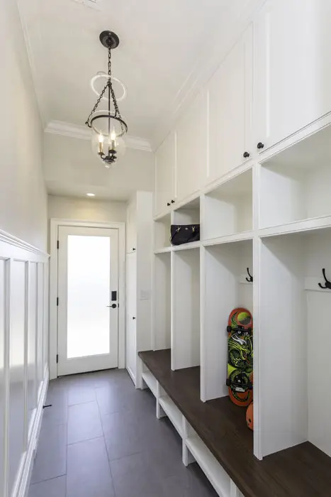 White entryway with bell jar type chandelier, rollerblades in the casework and black coat hooks