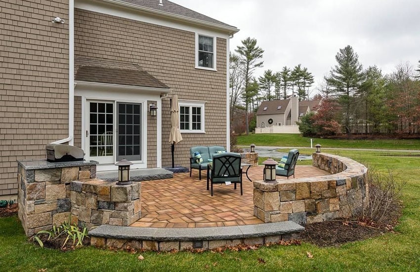 Backyard raised stone patio with small wall and outdoor lighting