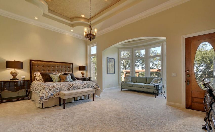 Beautifully decorated tan bedroom with sitting area and high ceiling