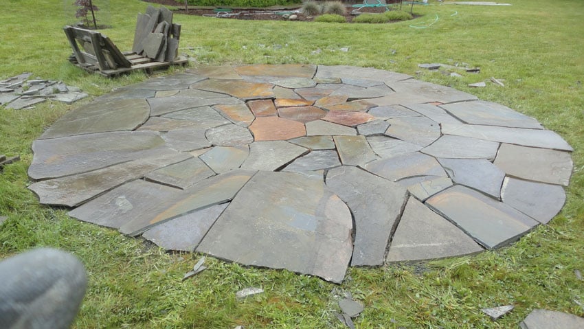 Cut stone patio circle in backyard surrounded by grass