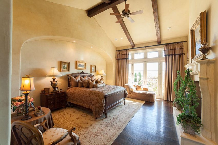 Mediterranean style bedroom with tan painted walls exposed beam vaulted ceiling and fireplace