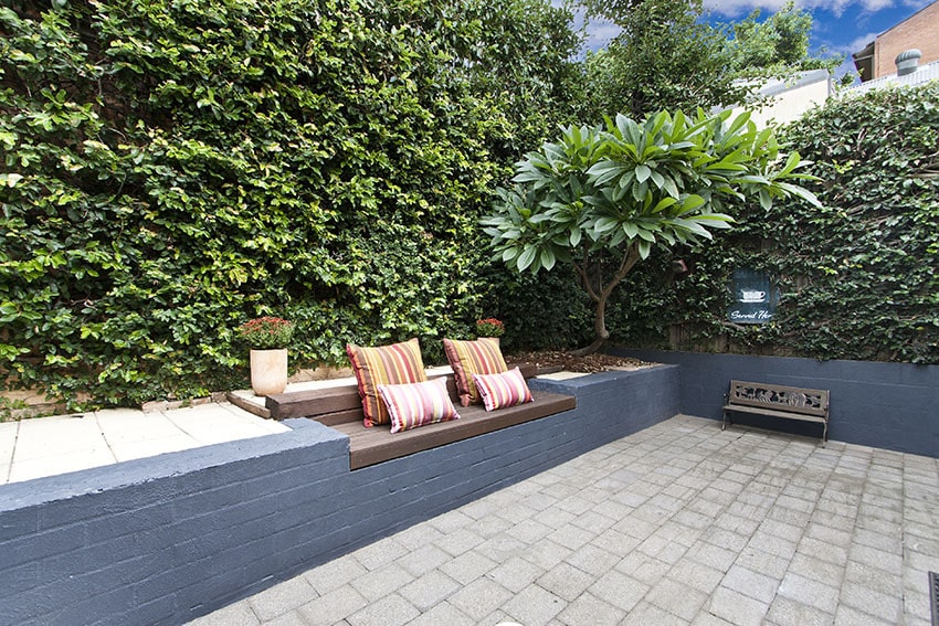 Paver patio with rustic wood bench and hedges in backyard