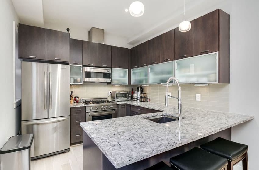 J shaped kitchen with black and white quartz countertops and dark brown cabinets