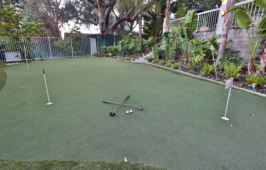 Large backyard putting green with tropical plants