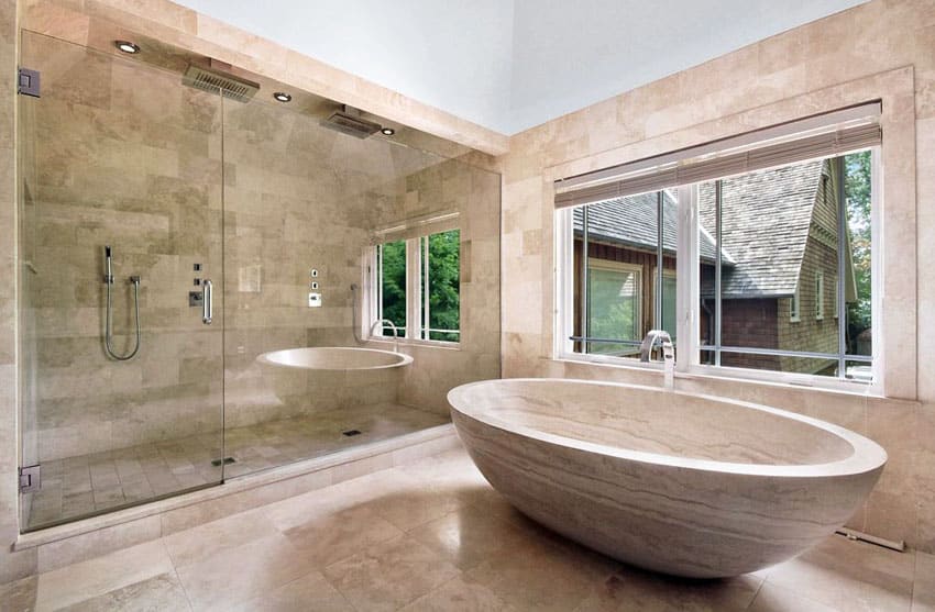 Walk-in glass shower with travertine tile, dual rainfall showerheads and custom stone tub