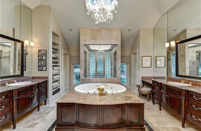 Luxury bathroom with dual dark wood custom vanities, enclosed tub with brown marble surface