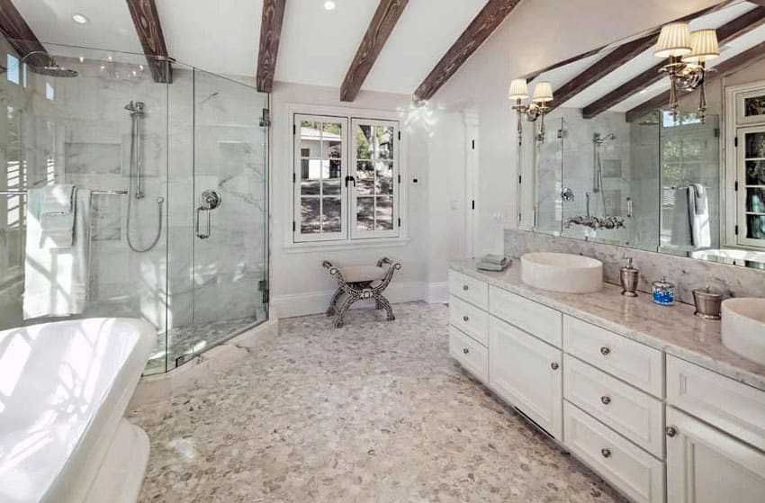 Luxury bathroom with exposed beam ceiling, stone pebble floors, soaking tub and vessel sinks