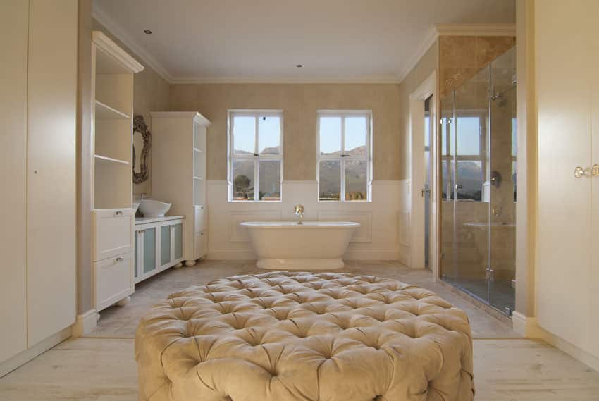 bathroom in new construction house with white painted and glass vanity, relaxing tub and plush ottoman