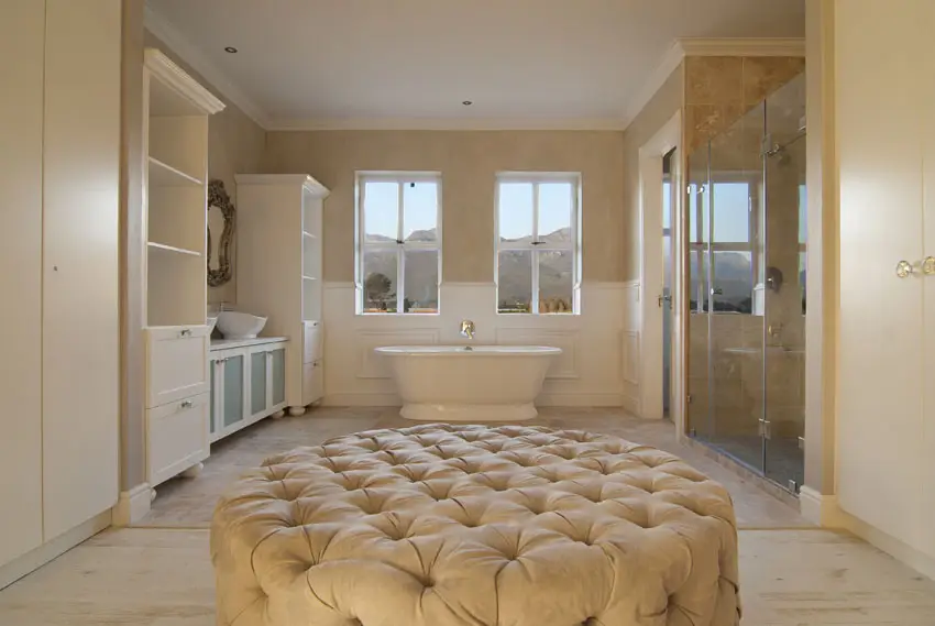 Master bathroom in new construction house with white vanity, freestanding tub and plush ottoman