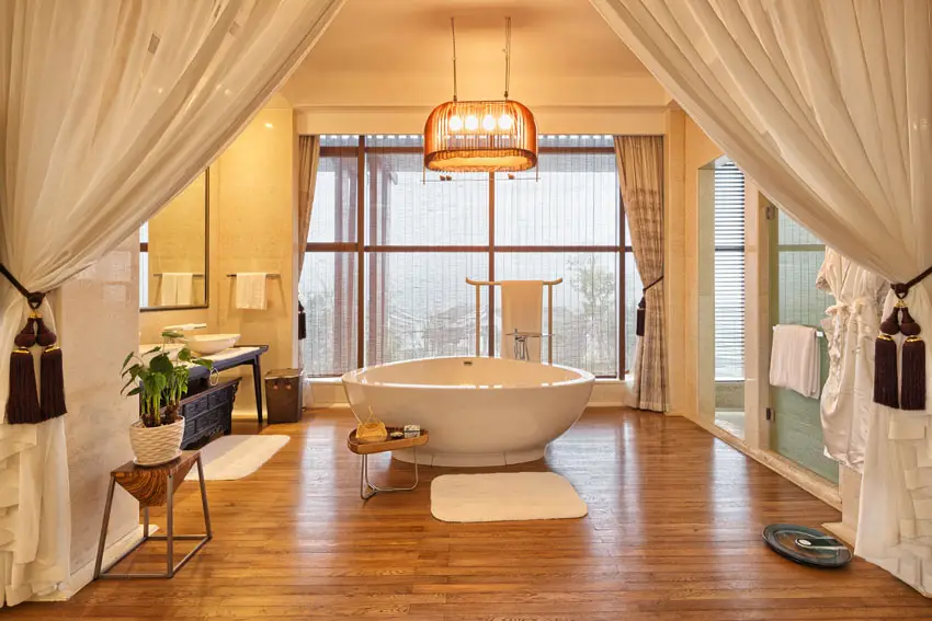 Master bathroom with large curtains, wood floors and freestanding tub