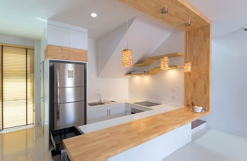 Small white kitchen with wood counter breakfast bar and pendant lights