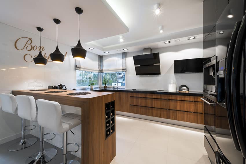 Trendy kitchen with wood counter peninsula, white leather bar stools and black pendant lights