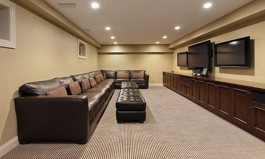 Basement living room with multiple tvs and long brown leather couch with ottoman