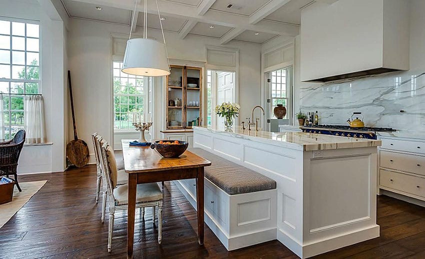 Beautiful white kitchen with marble counters and backsplash with island and long bench seat