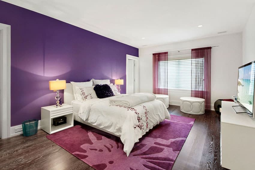 Bedroom with bold purple accent wall and white paint with white furniture