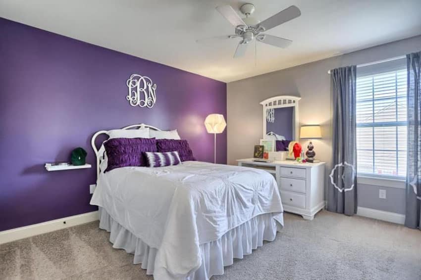 Bedroom with purple accent wall and sand color walls with light carpet