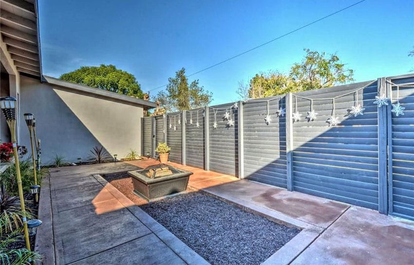 Patio with gravel center area with hanging lights on the gray fence