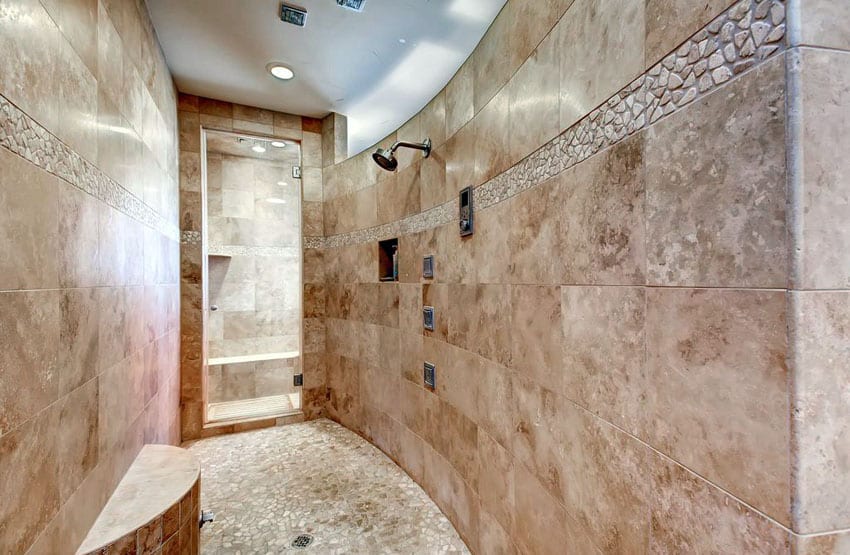 Curved travertine large format tiled shower with pebble floor tile and round bench