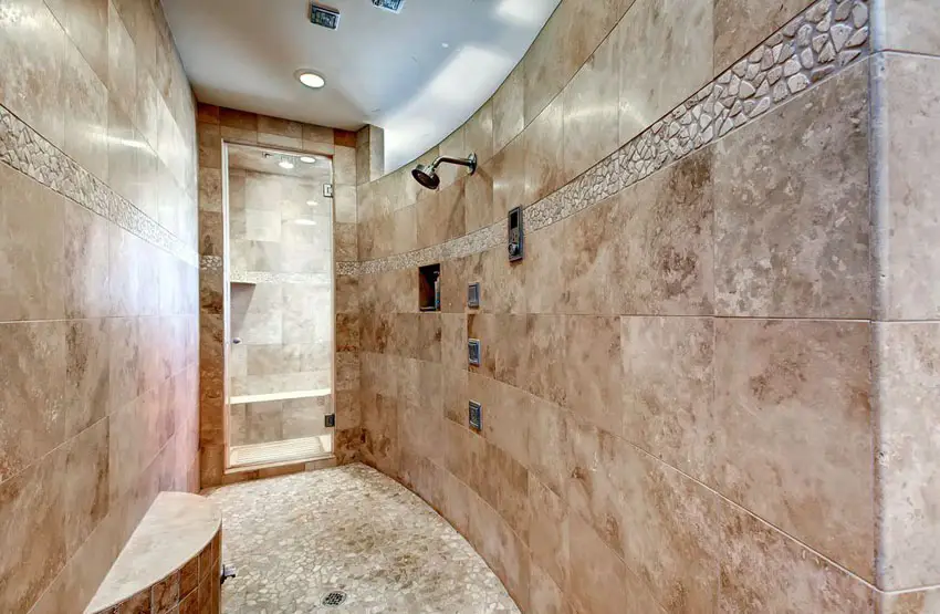 Curved travertine shower with pebble floor tile and round bench
