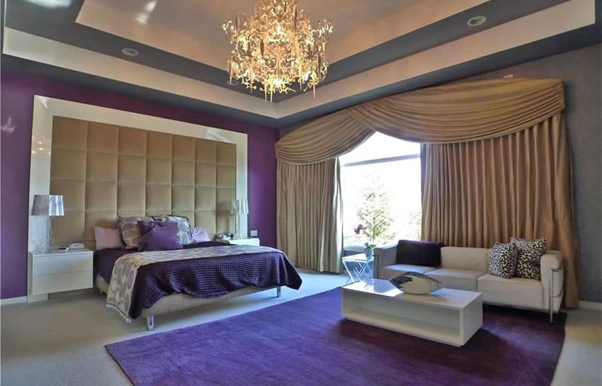 Luxury master bedroom with purple accent wall large area rug plush headboard and chandelier
