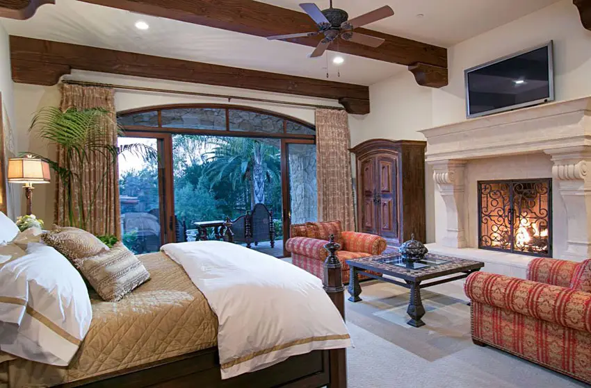 Luxury master bedroom with stone fireplace wood beam ceilings and outdoor balcony