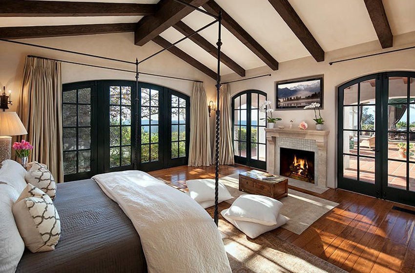 Luxury Mediterranean master bedroom with fireplace french doors and wood flooring