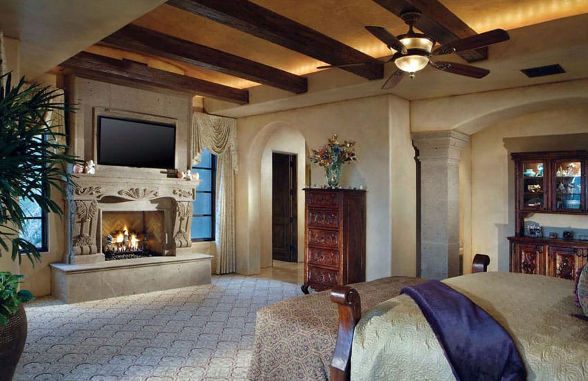 bedroom with stone intricate carved fireplace, exposed beam ceiling and wall columns