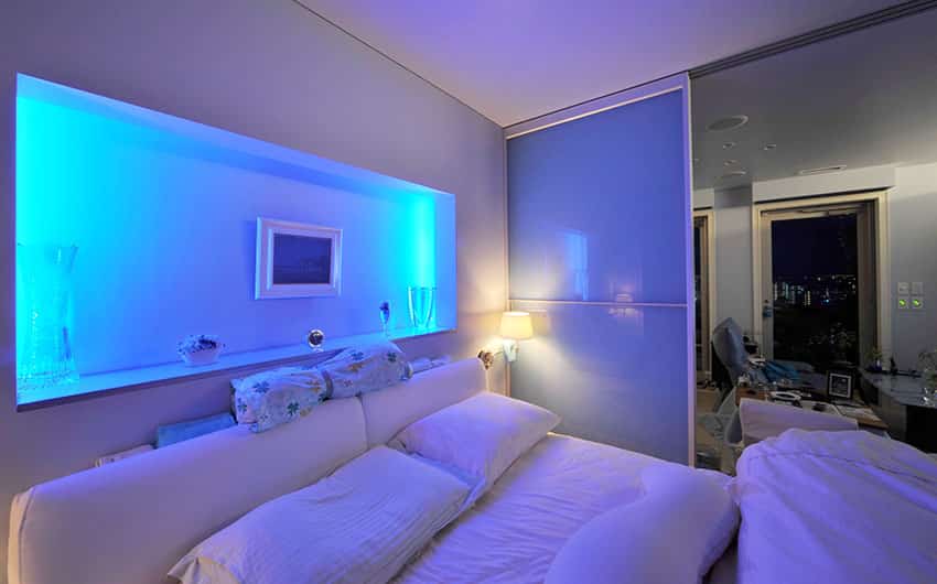 Modern bedroom with purple walls mood lighting from wall alcove and white furnishings