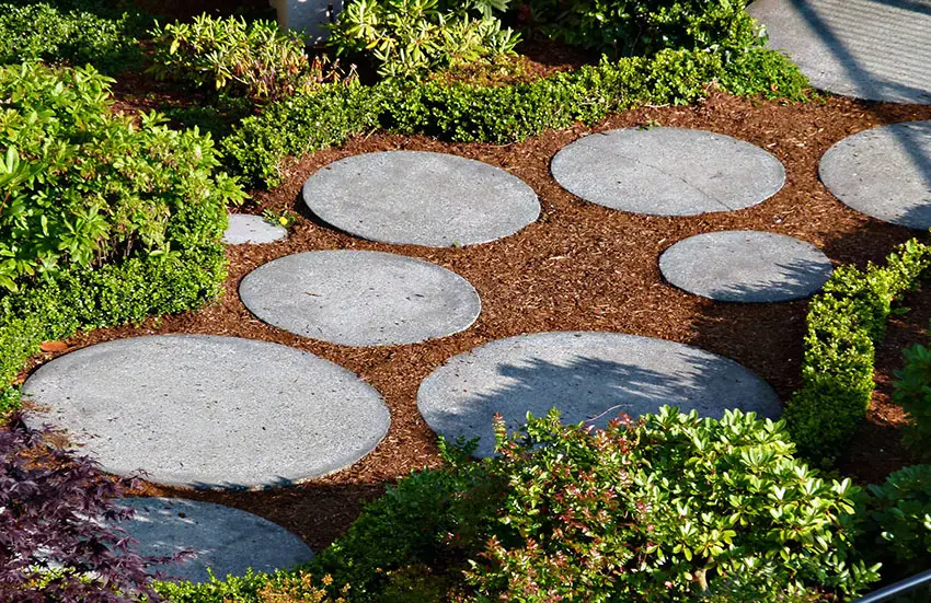 Round garden pavers surrounded by bark and bushes