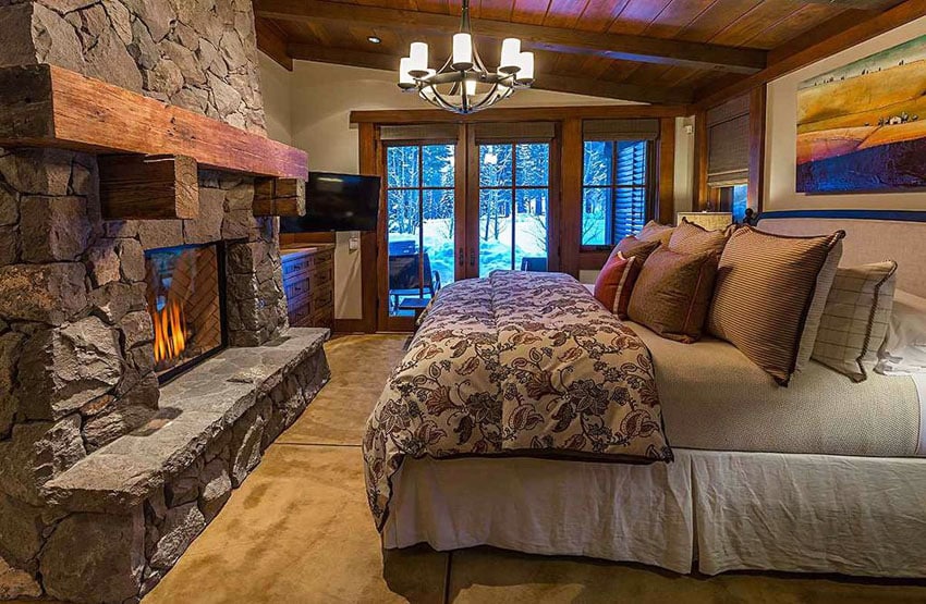 Rustic craftsman style bedroom with rough stone fireplace and forest views