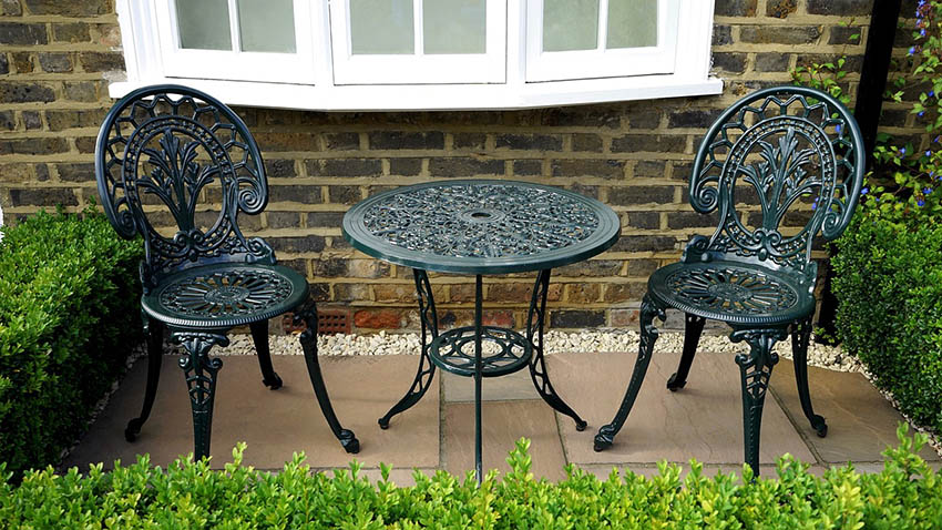 Small garden patio with white gravel border and wrought iron furniture set