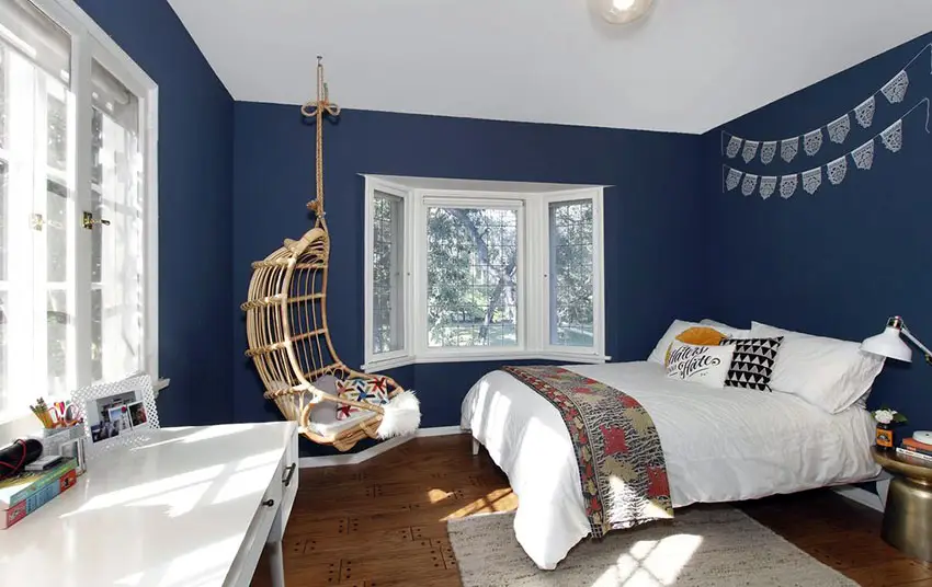 Bedroom with hanging rattan chair and blue wall design and windows with white trim