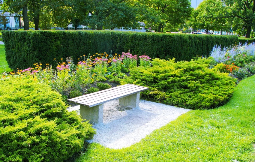 Wood slat bench in gravel surrounded by garden