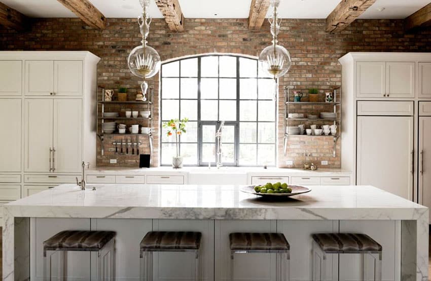 Beautiful kitchen with large island with Statuario polished marble countertops, white cabinets and brick accent wall