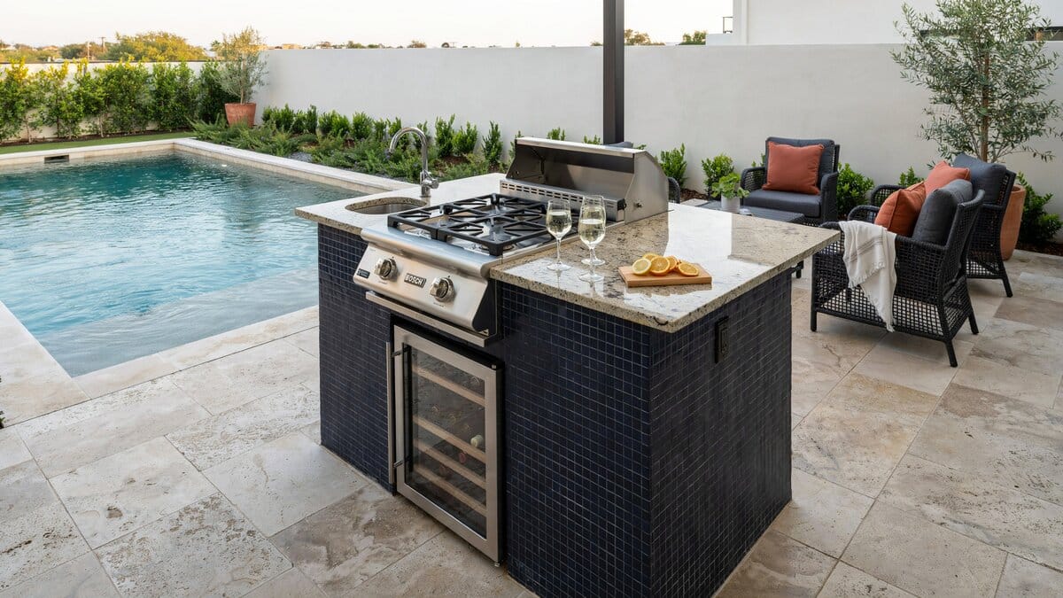 Poolside outdoor kitchen with a blue tiled base and black rattan lounge furniture
