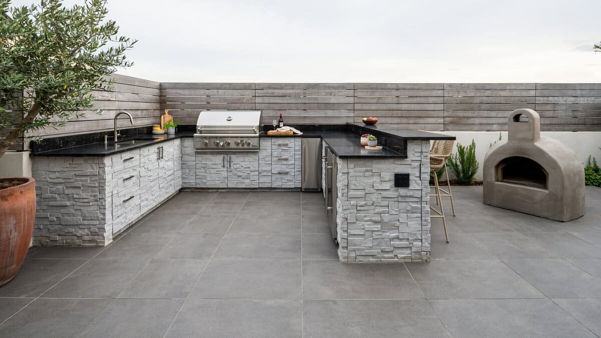L-shaped outdoor kitchen with gray stone cladding and a concrete oven on pavers
