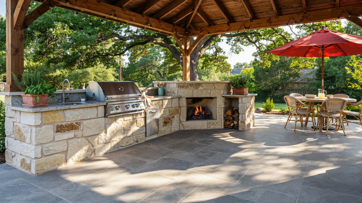 Stone block outdoor kitchen joined to a fireplace with a red patio umbrella