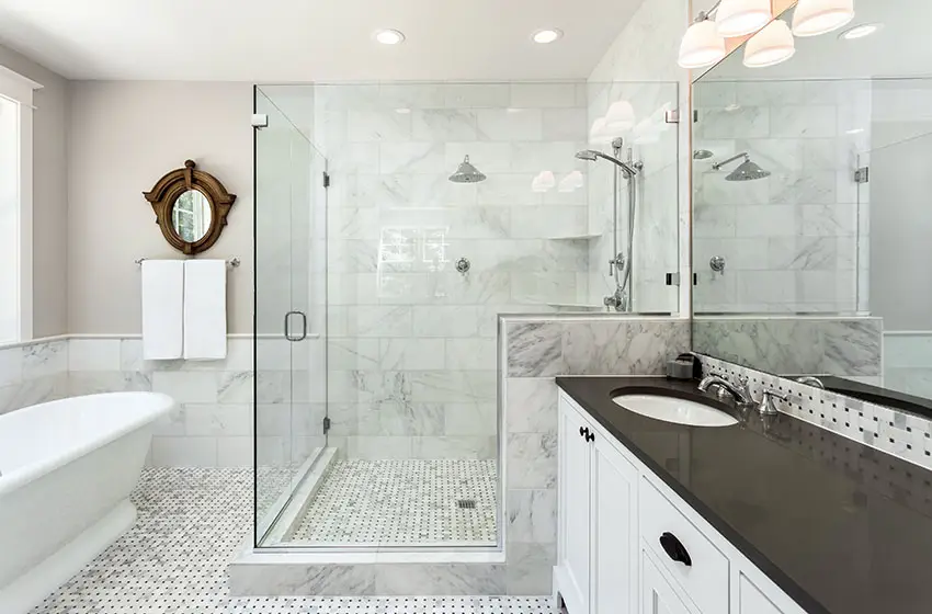 White marble bathroom with prominent glass shower, white vanity with black countertops