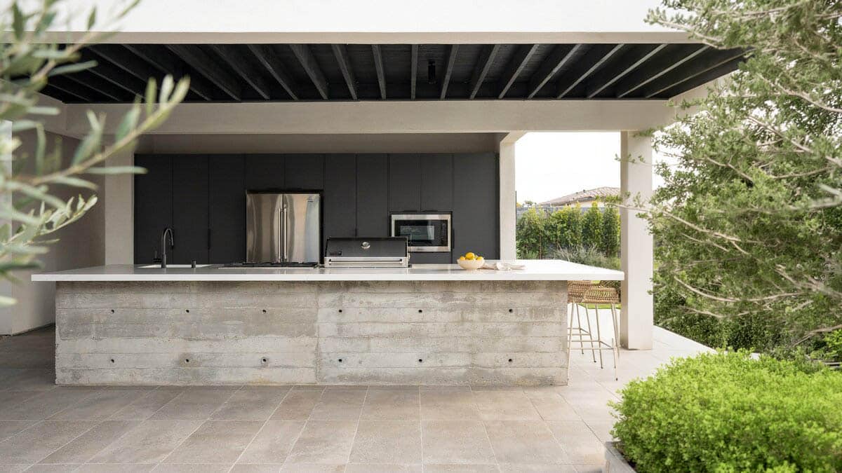 Raw concrete island kitchen with a stainless refrigerator under a covered patio
