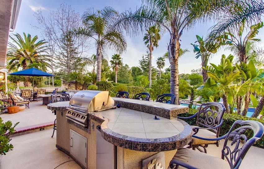 Outdoor kitchen with curved countertop and bar stool seating overlooking swimming pool