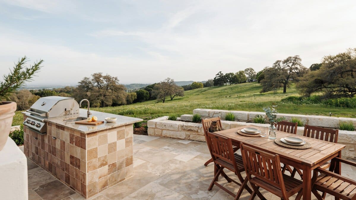 Simple patio kitchen with beige granite counters beside a hillside dining set