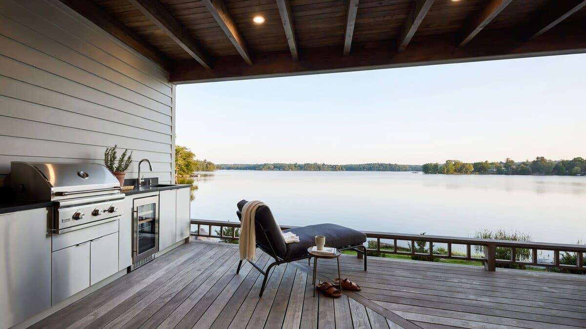 Sleek stainless steel outdoor kitchen with black counters overlooking a calm lake
