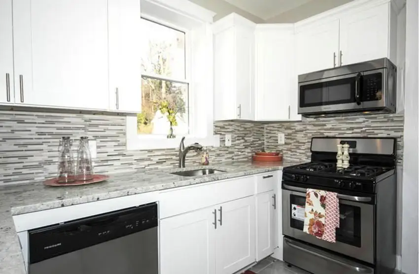 Kitchen with vertical tile backsplash, cabinets with chrome handles and white drawers