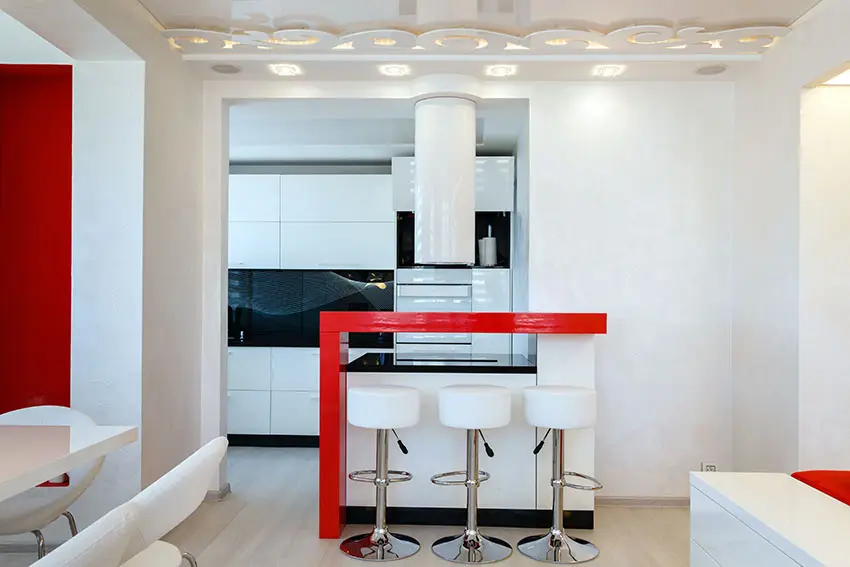 Kitchen with red bar peninsula, white bar chairs with metal legs and laminate floors